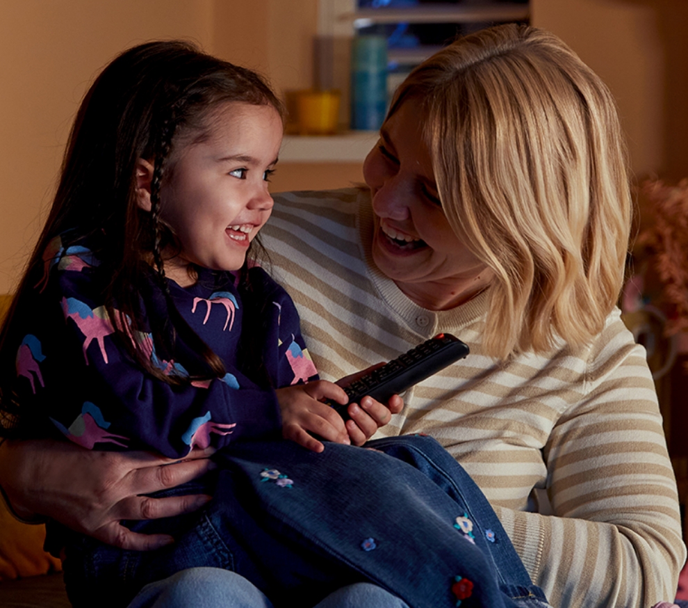 A mother and her young daughter sat on the sofa laughing as they’re making energy savings at home with Utilita High 5.